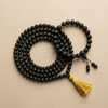 Black beaded necklace with a yellow tassel on a beige background
