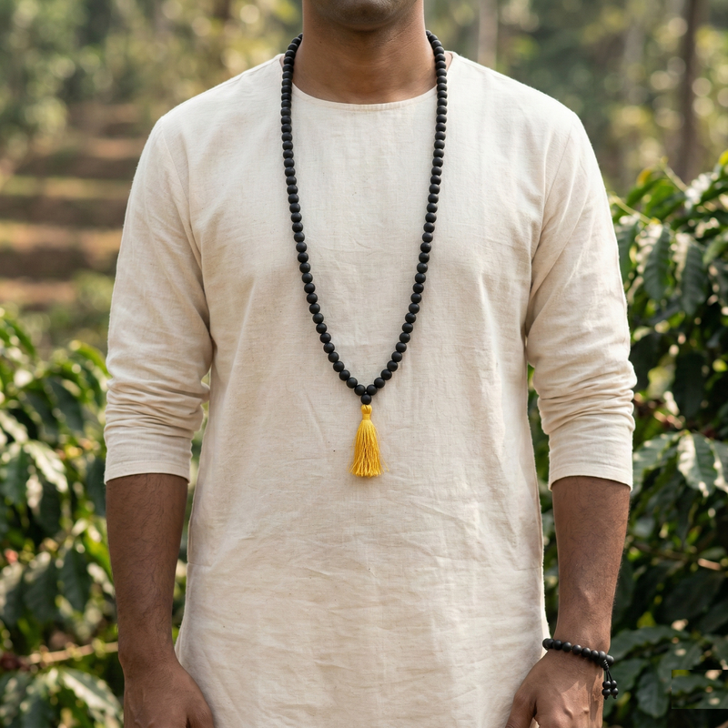 Person wearing a long black beaded necklace with a yellow tassel outdoors.