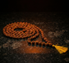 Brown beaded necklace with a yellow tassel on a dark textured surface
