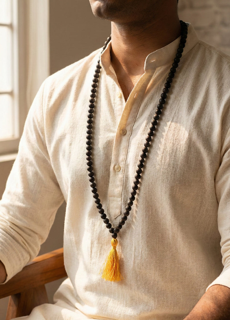 Man wearing a beige kurta with a long black beaded necklace and yellow tassel.