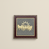 Framed artwork with a gold design on a gray background, mounted on a beige wall.