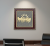 Decorative wall art with a gold design of horses and a sun on a gray background, framed in brown, in an office setting.