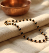 Black beaded necklace with gold accents on a beige fabric background