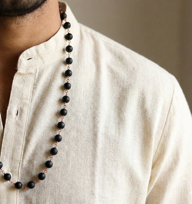 Man wearing a beige kurta with a long black beaded necklace.