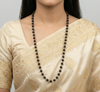 Woman wearing a beige saree with gold patterns and a long black beaded necklace.