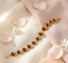 Gold bracelet with brown beads on a soft pink fabric background with flower petals