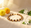 Bracelet with gold and brown beads on a beige surface with flowers and leaves.