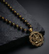 Black beaded necklace with a gold pendant on a dark stone surface