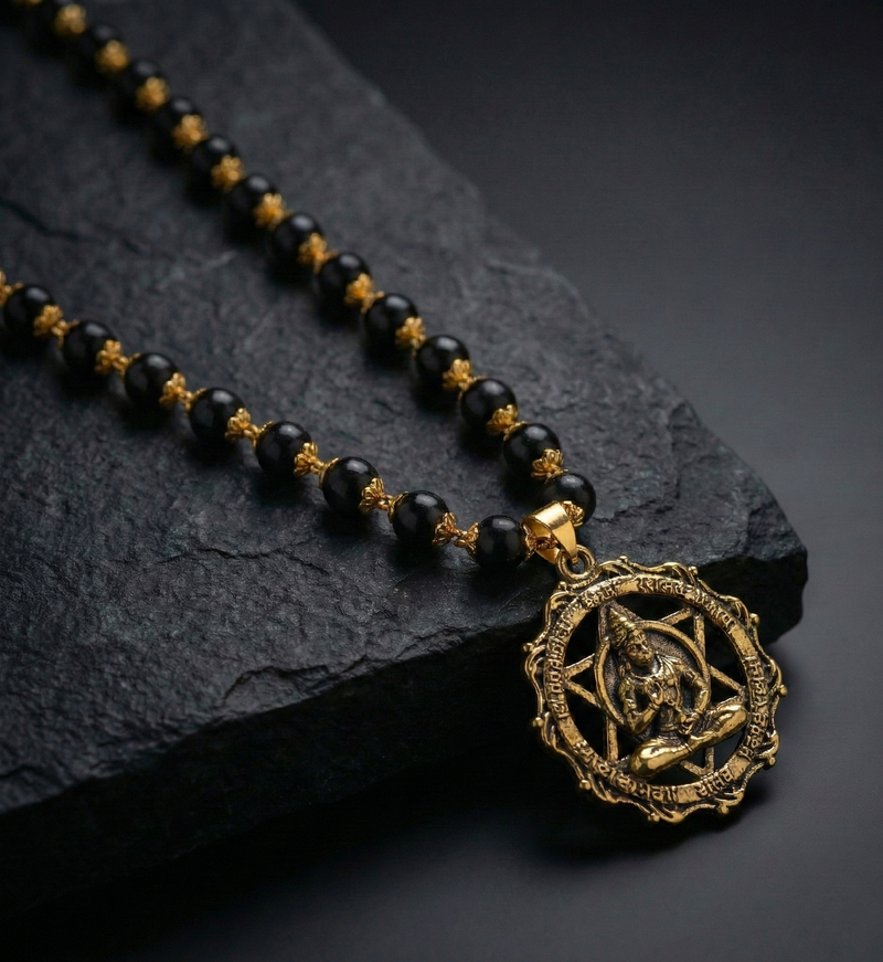 Black beaded necklace with a gold pendant on a dark stone surface