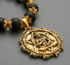 Necklace with black beads and gold medallion on a gray background