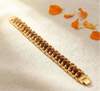Bracelet with brown beads and gold chain on a light fabric background with orange petals.