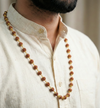 Man wearing a long beaded necklace on a plain background