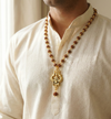 Man wearing a beaded necklace with a gold pendant on a plain background