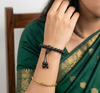 Person wearing a green saree with gold patterns, holding a black beaded bracelet.