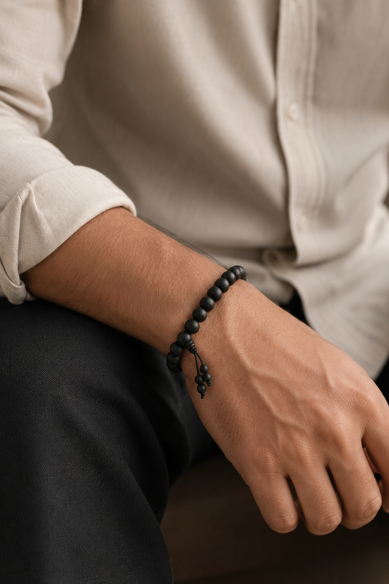 Person wearing a black beaded bracelet on a neutral background
