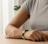 Person wearing a beaded bracelet on a wooden surface with a neutral background