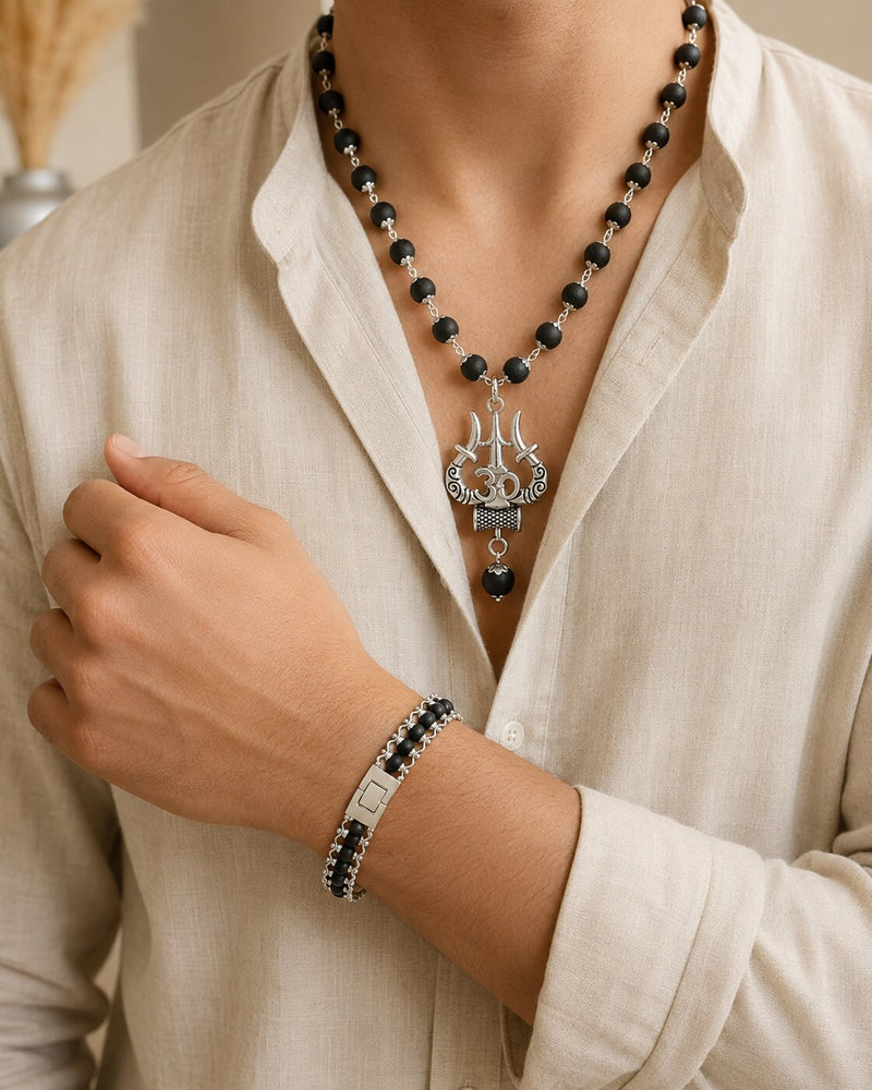 Person wearing a black beaded necklace and bracelet with a silver pendant on a beige background