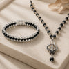 Black beaded necklace with silver pendant and bracelet on a beige surface