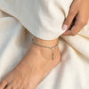 Silver anklet on a foot with white fabric background