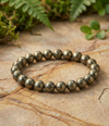 Pyrite beaded bracelet on a stone surface with green foliage