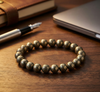 Bronze beaded bracelet on a wooden surface with a notebook and pen in the background