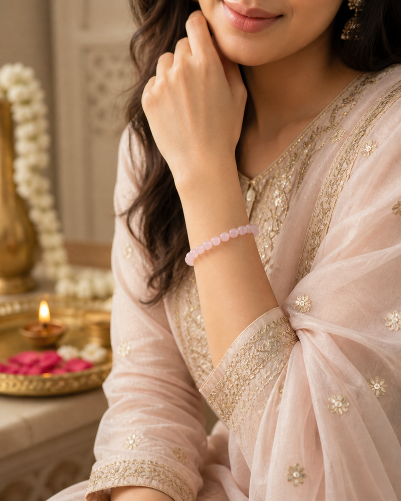 Woman wearing a light pink saree with gold embroidery, holding her hand to her face.