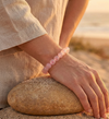 Person wearing a pink beaded bracelet on a sandy beach