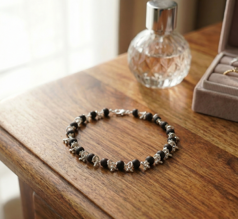 Black and silver beaded bracelet on a wooden surface with a glass bottle and jewelry box in the background.