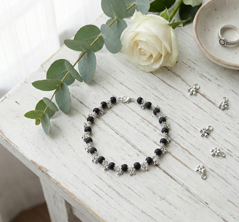 Black beaded bracelet on a white wooden surface with a white rose and green leaves.