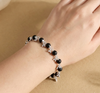 Black beaded bracelet with silver accents on a wrist against a beige background