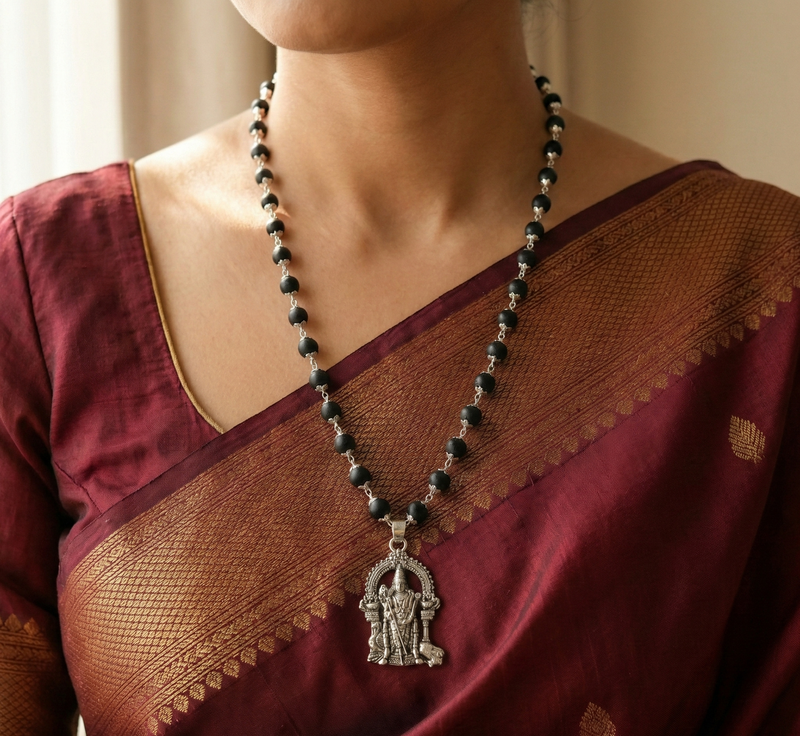 Person wearing a maroon saree with a black beaded necklace and silver pendant.