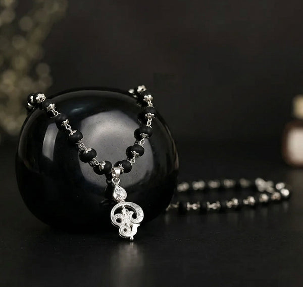 Black beaded necklace with silver pendant on a dark background