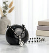 Black and silver beaded necklace on a black sphere with books and plants in the background