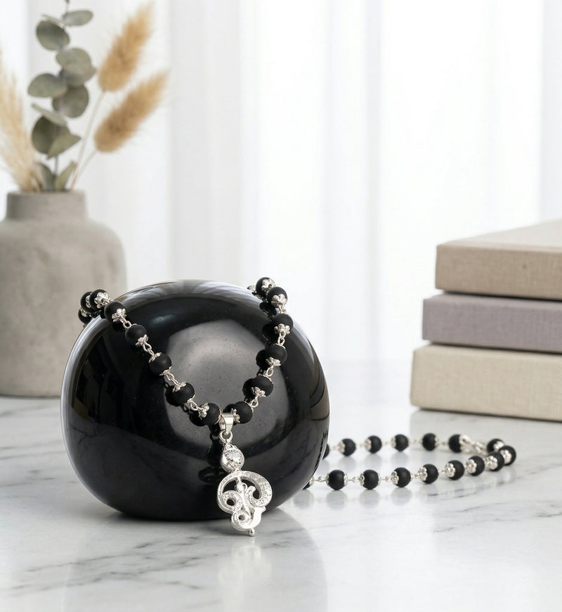 Black and silver beaded necklace on a black sphere with books and plants in the background