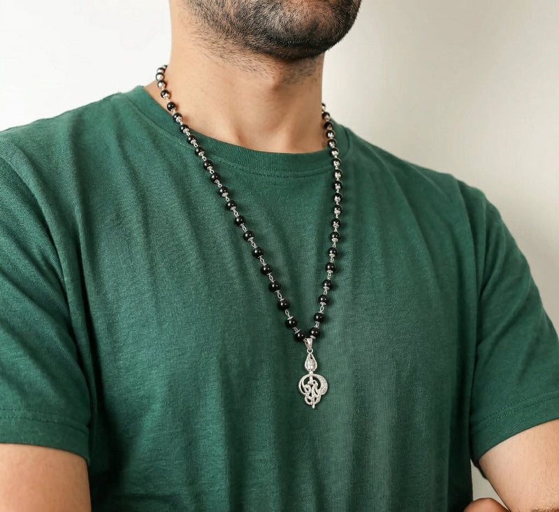 Man wearing a green t-shirt with a black beaded necklace featuring a silver pendant.