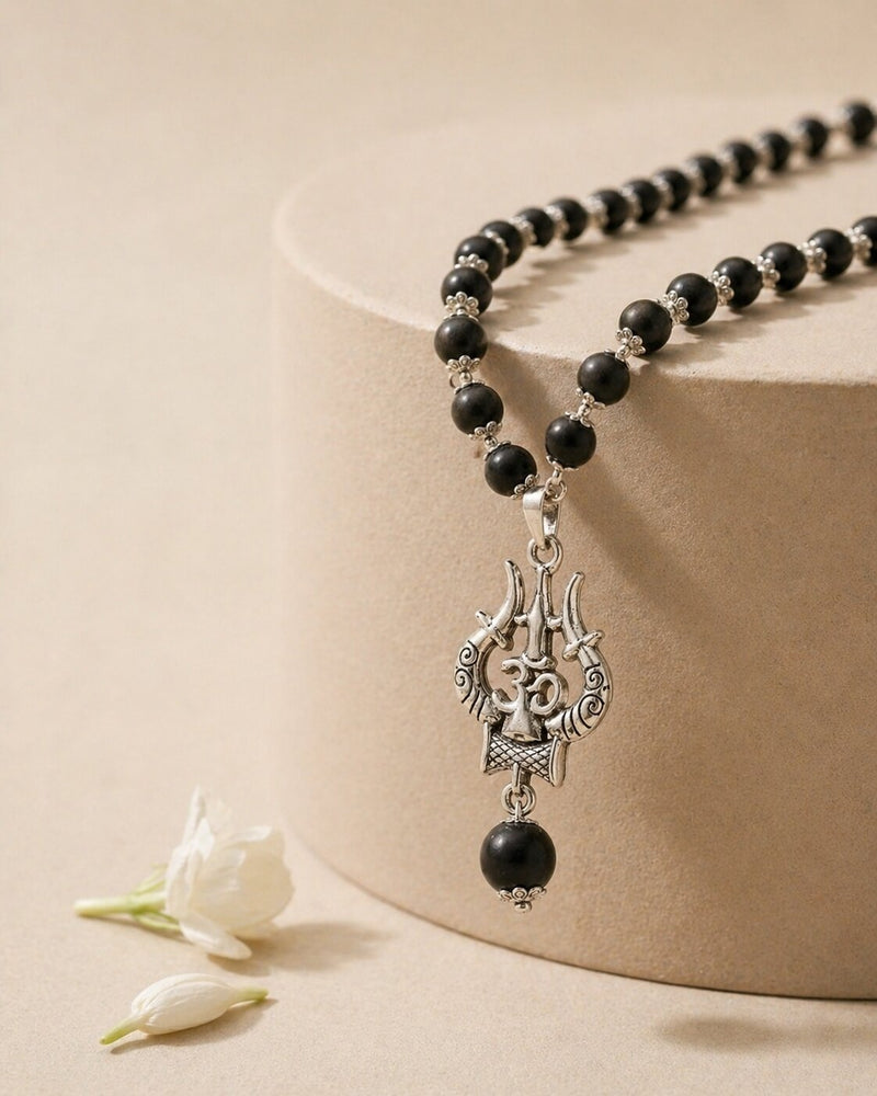 Black beaded necklace with a silver pendant on a beige surface with a white flower.