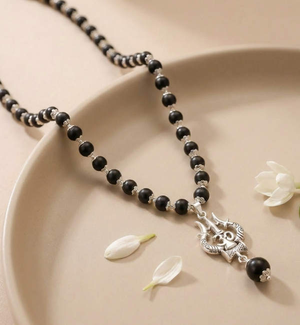 Black beaded necklace with a silver pendant on a beige plate with flowers