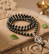 Black beaded necklace with a silver pendant on a textured stone surface with a candle in the background.