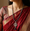 Person wearing a red saree with a black beaded necklace and silver pendant.
