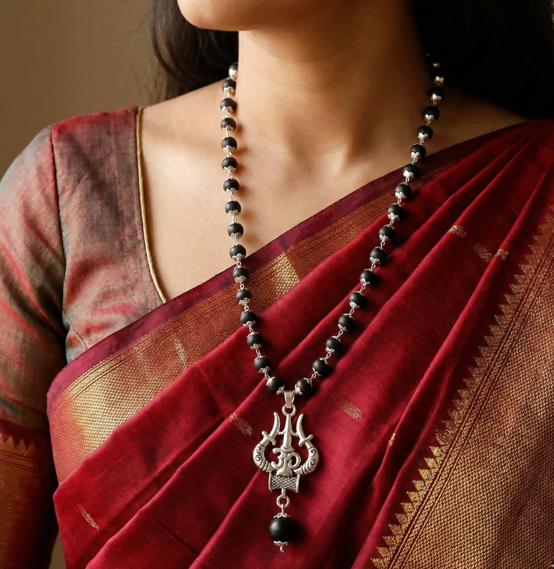 Person wearing a red saree with a black beaded necklace and silver pendant.