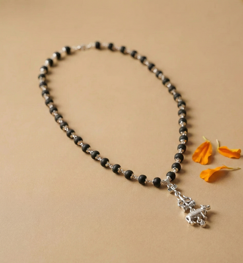 Black beaded necklace with a silver charm on a beige background