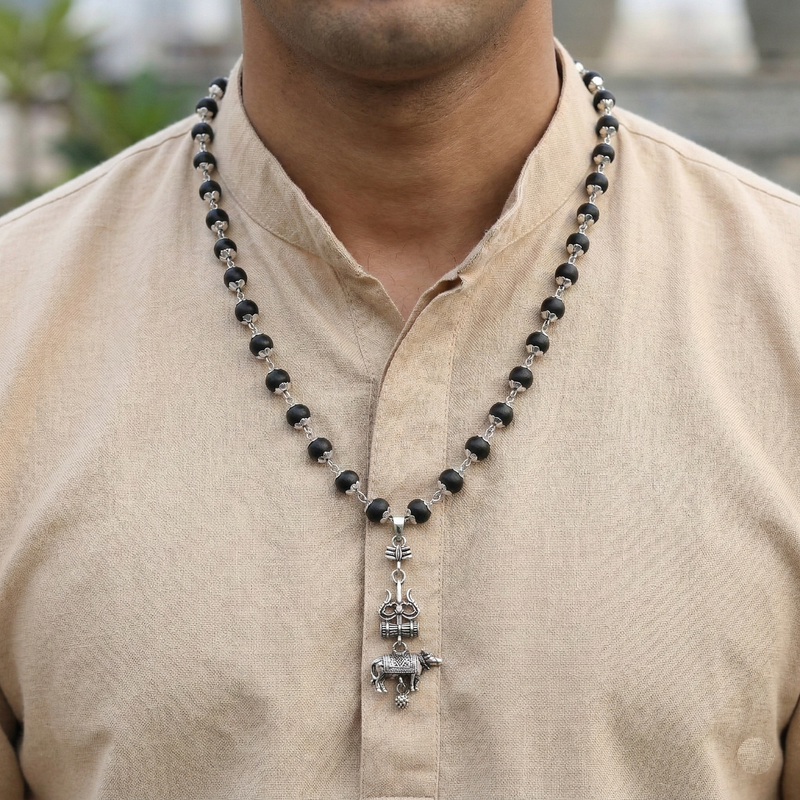 Man wearing a black beaded necklace with a silver pendant on a beige shirt.