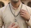 Man wearing a beaded necklace with a decorative pendant against a blurred background