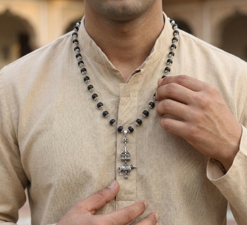 Man wearing a beaded necklace with a decorative pendant against a blurred background