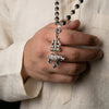 Hand holding a silver rosary with a rhinoceros pendant against a beige background
