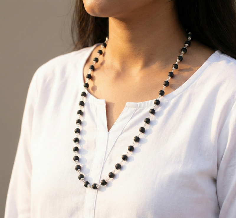 Person wearing a long black beaded necklace against a neutral background