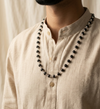 Person wearing a black beaded necklace with a beige shirt against a neutral background