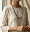 Person wearing a long black beaded necklace against a neutral background