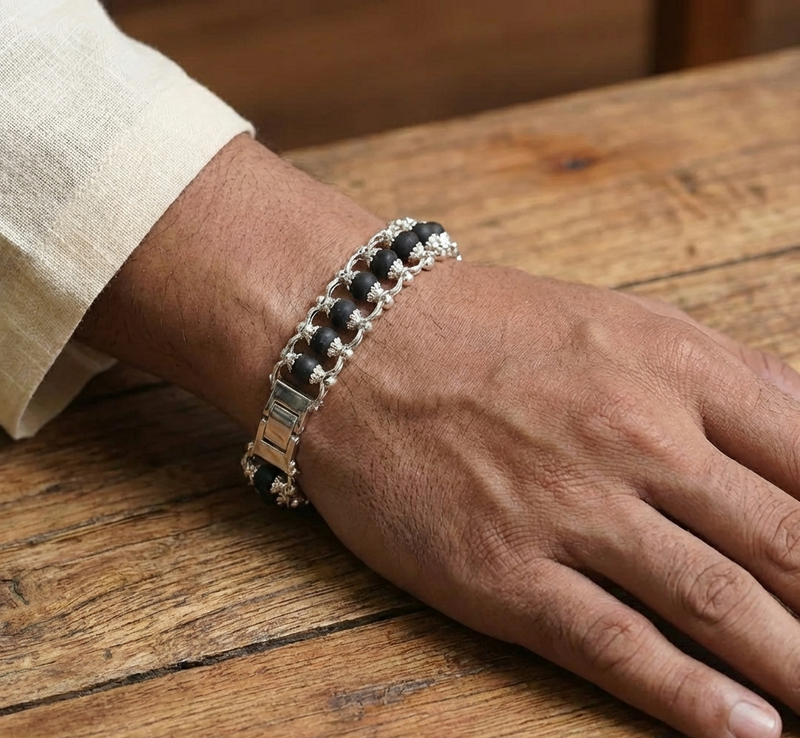 Hand wearing a black and silver bracelet on a wooden surface