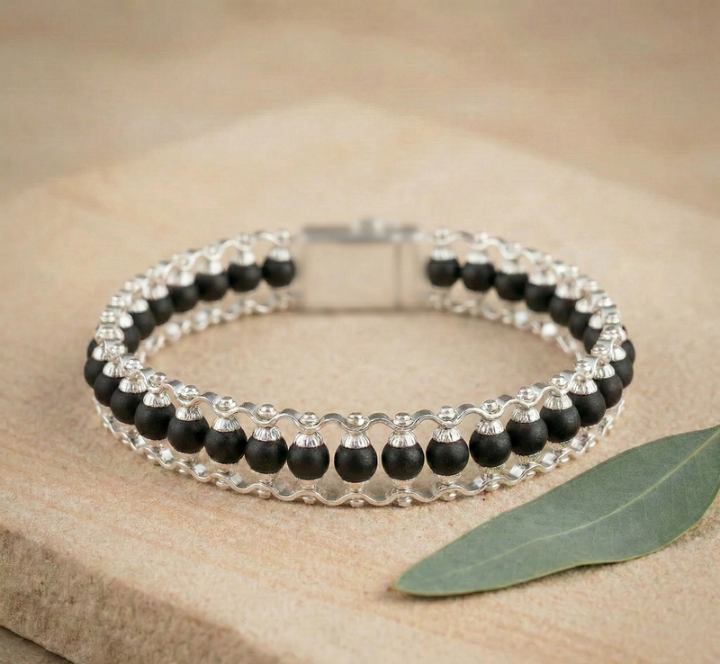 Black and silver beaded bracelet on a beige surface with a leaf